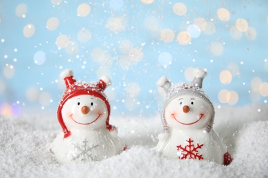 Photo of Decorative snowmen on artificial snow against blurred festive lights