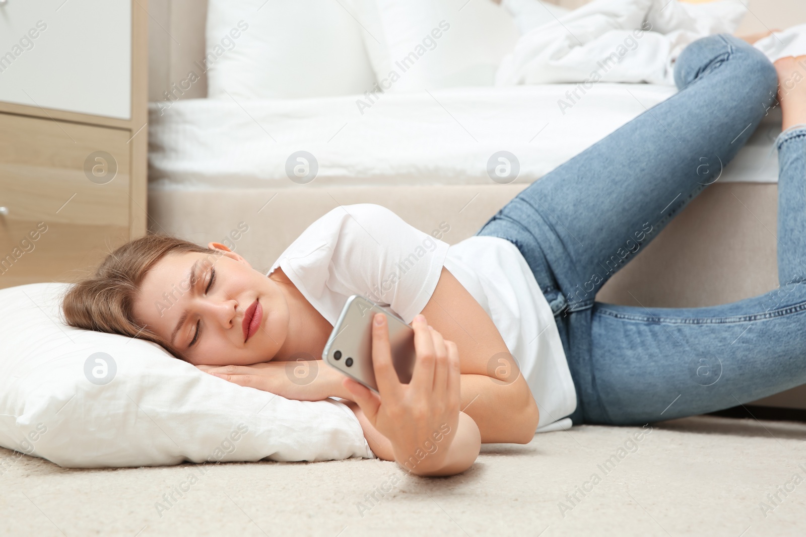 Photo of Lazy young woman with smartphone lying on floor at home