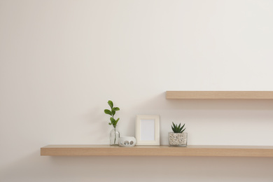 Photo of Wooden shelves with plants and photo frame on light wall