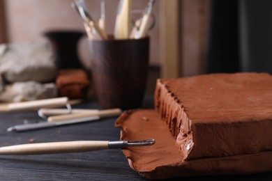 Photo of Clay and modeling tool on dark gray wooden table in workshop, closeup