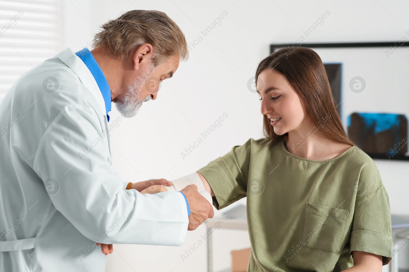 Photo of Orthopedist applying bandage onto patient's elbow in clinic