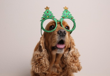 Photo of Adorable Cocker Spaniel dog in party glasses on light background