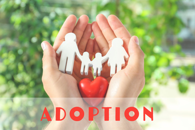 Young man holding wooden family figure and red heart in his hands against blurred background, closeup. Child adoption concept