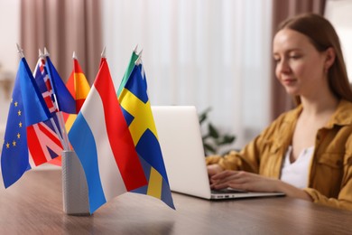 Photo of Woman working with laptop at table indoors, focus on different flags