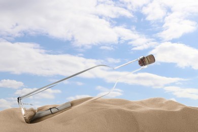 Photo of Corked glass bottle with rolled paper note on sand against sky