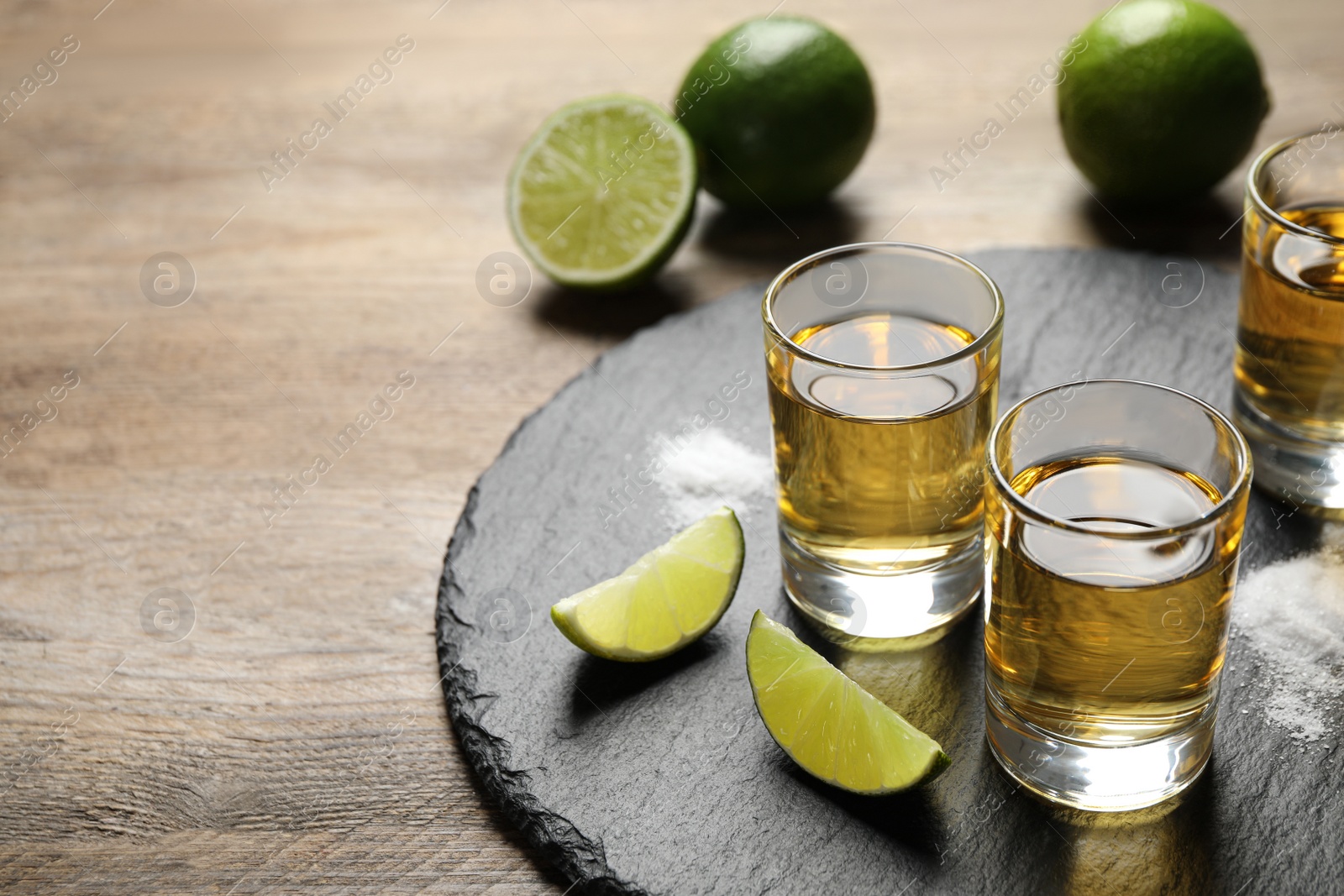 Photo of Mexican Tequila shots, lime slices and salt on wooden table