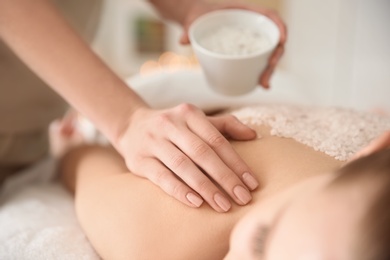 Beautiful young woman having massage with body scrub in spa salon