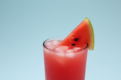 Photo of Delicious drink with ice cubes and piece of fresh watermelon on light blue background
