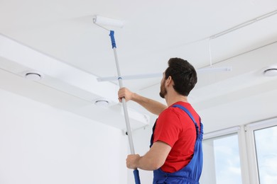 Photo of Handyman painting ceiling with roller in room, back view