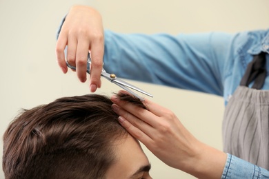 Barber making stylish haircut with professional scissors in beauty salon, closeup