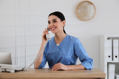 Receptionist talking on phone at countertop in hospital