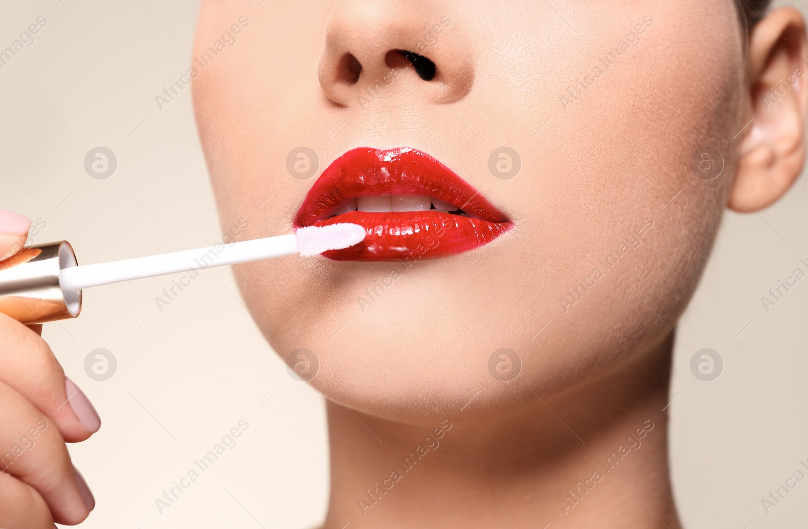 Photo of Beautiful woman applying red gloss on lips against color background, closeup