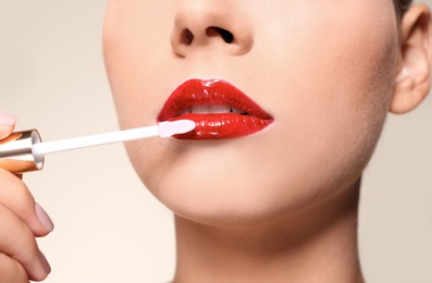 Photo of Beautiful woman applying red gloss on lips against color background, closeup