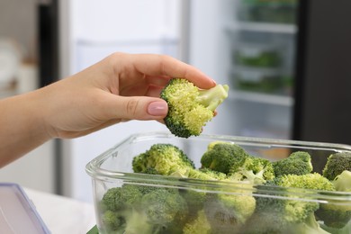 Photo of Woman putting green broccoli into glass container in kitchen, closeup. Food storage