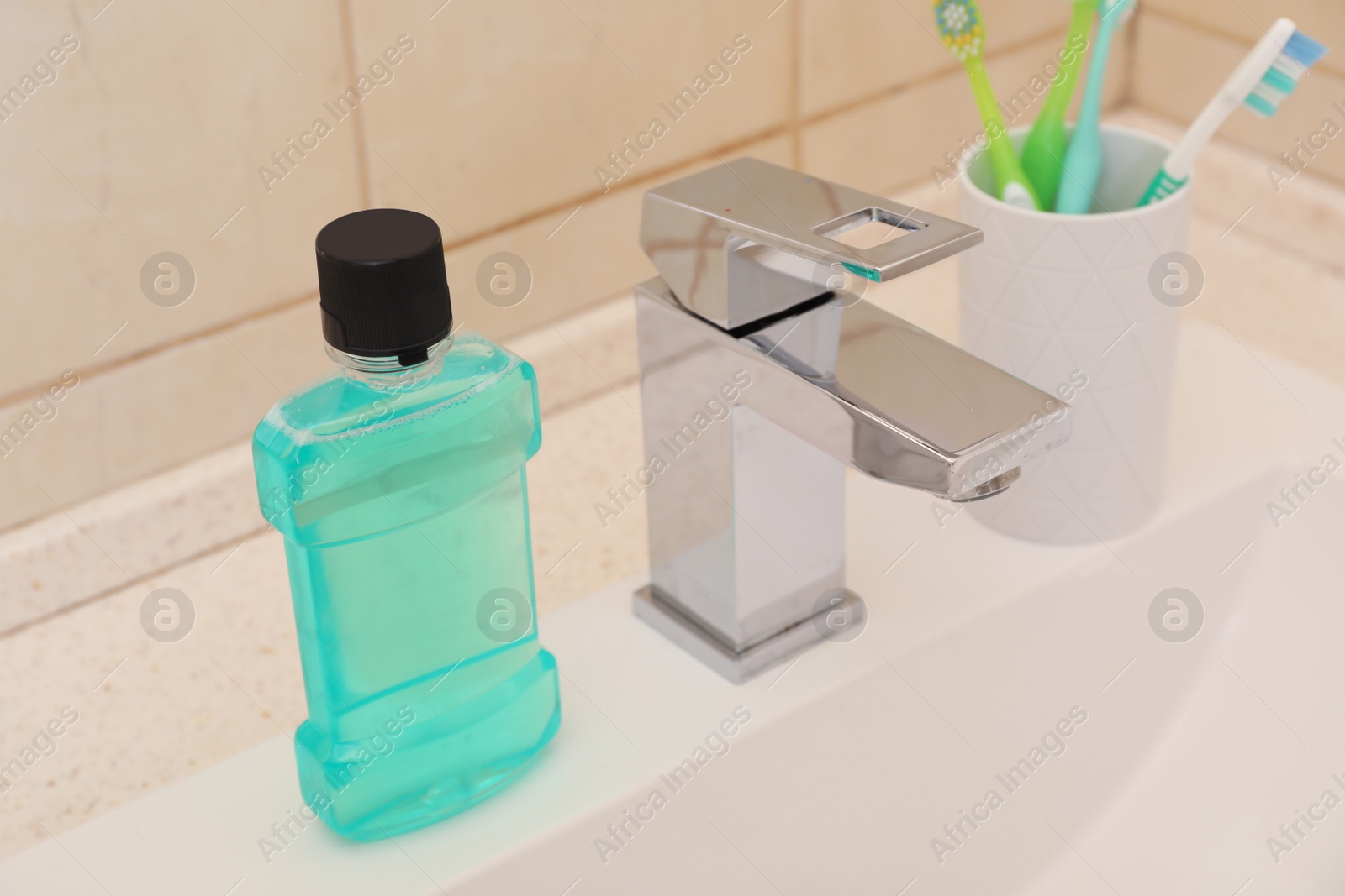 Photo of Mouthwash and holder with toothbrushes on sink in bathroom. Teeth and oral care