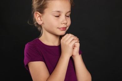 Photo of Girl with clasped hands praying on black background, closeup