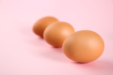 Raw chicken eggs on pink background, closeup. Space for text