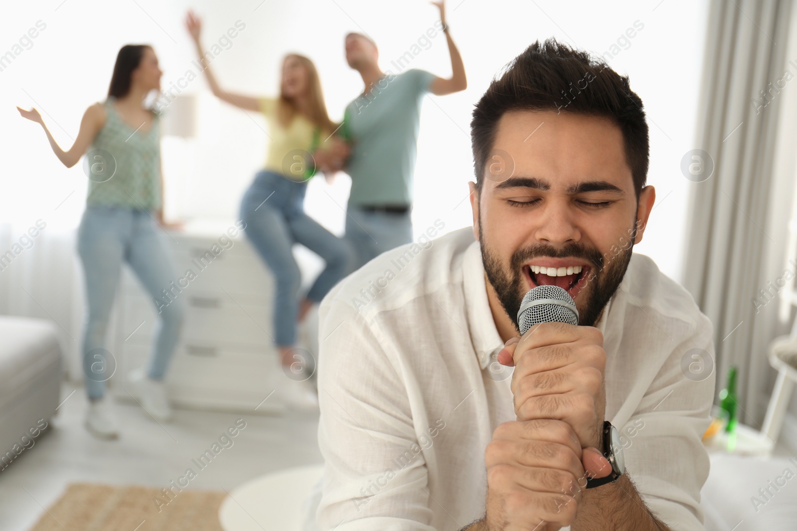 Photo of Young man singing karaoke with friends at home