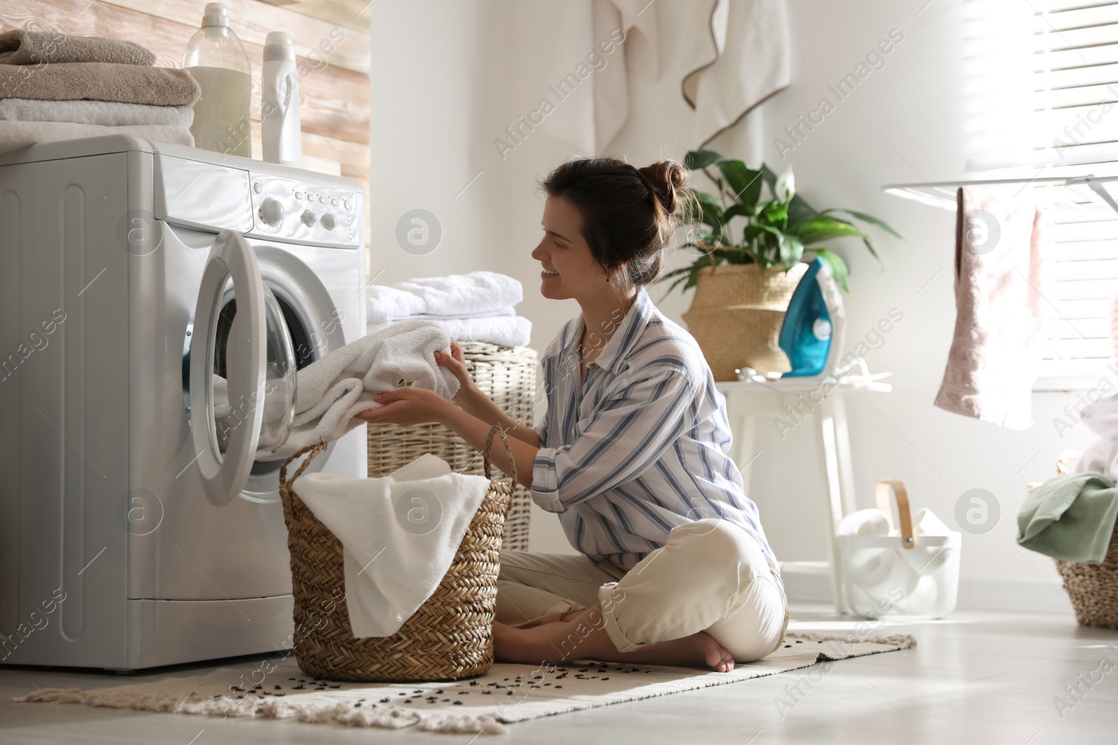 Photo of Young woman taking laundry out of washing machine at home