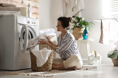 Photo of Young woman taking laundry out of washing machine at home