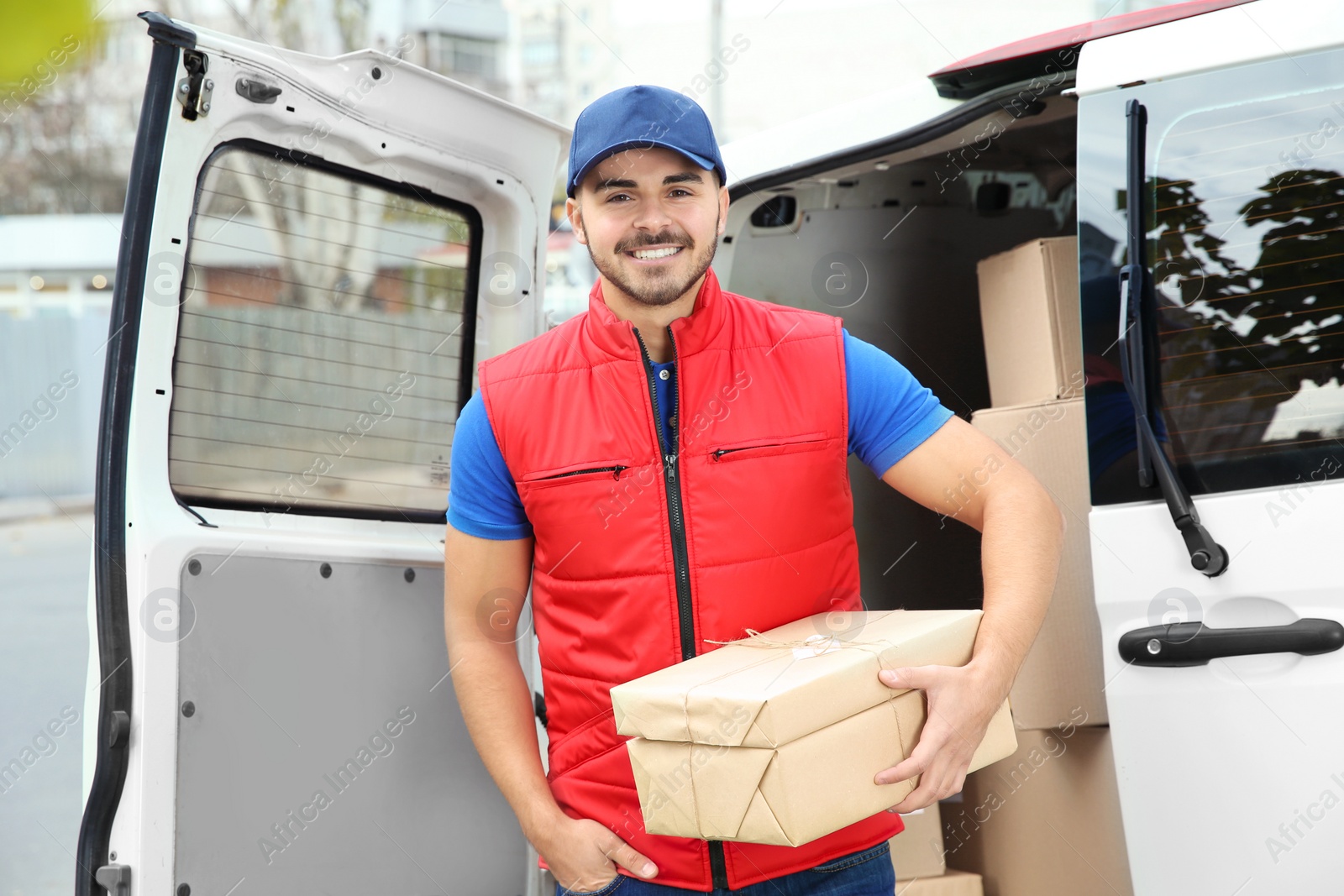 Photo of Young courier with parcels near delivery van outdoors