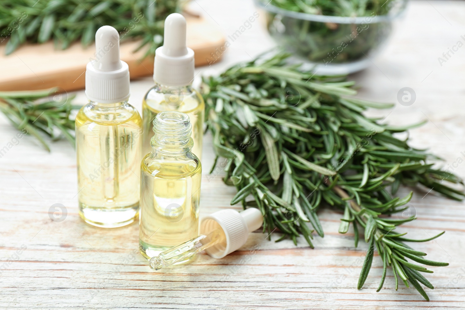 Photo of Bottles of rosemary essential oil on white wooden table