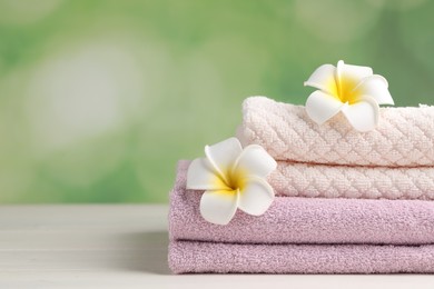 Photo of Closeup view of soft folded towels and plumeria flowers on white wooden table, space for text