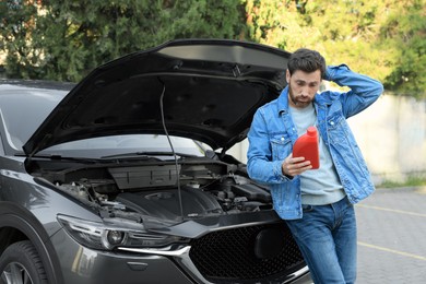 Photo of Puzzled man holding red container of motor oil near car outdoors
