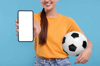 Photo of Happy soccer fan with ball showing smartphone on light blue background, closeup