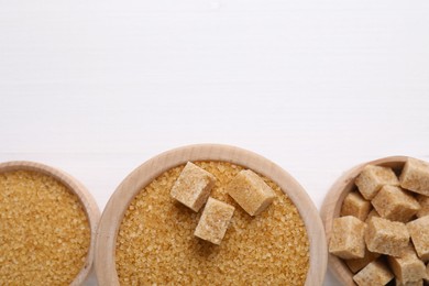 Different types of brown sugar in bowls on white table, flat lay. Space for text