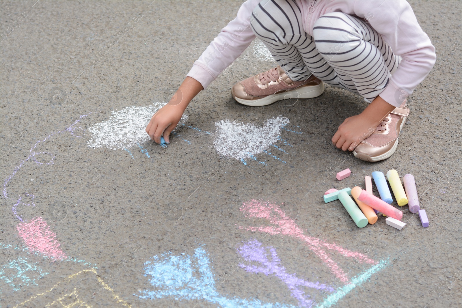 Photo of Little child drawing white clouds with chalk on asphalt, closeup