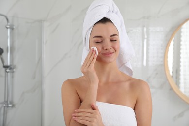 Photo of Beautiful young woman with hair wrapped in towel cleaning her face indoors