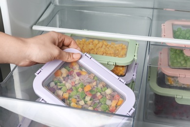 Woman taking box with vegetable mix from refrigerator, closeup