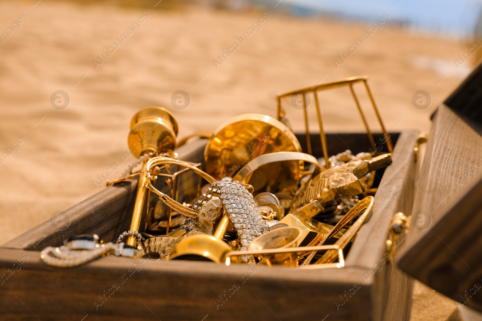 Photo of Open wooden treasure chest on sandy beach, closeup