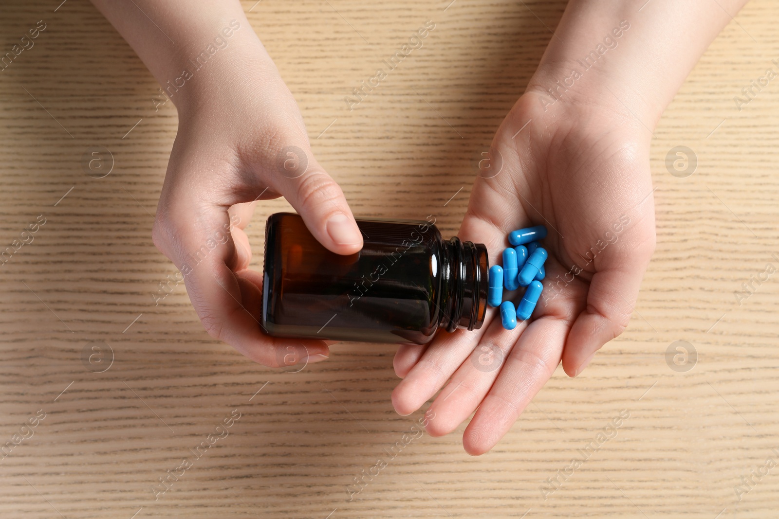 Photo of Woman pouring pills from bottle at wooden table, top view