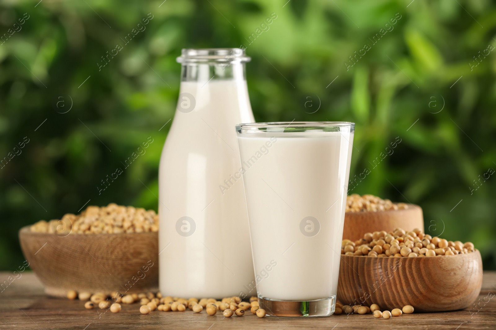 Photo of Fresh soy milk and grains on white wooden table against blurred background