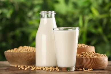 Fresh soy milk and grains on white wooden table against blurred background