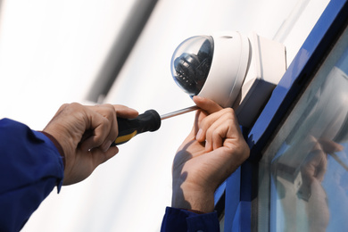 Technician installing CCTV camera on wall outdoors, closeup