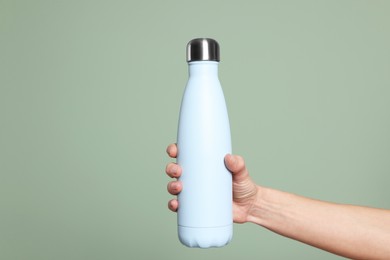 Woman holding thermo bottle on green background, closeup