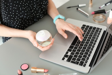 Young woman with makeup products using laptop at table. Beauty blogger