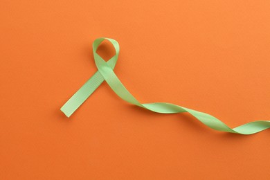 Photo of Light green awareness ribbon on orange background, top view