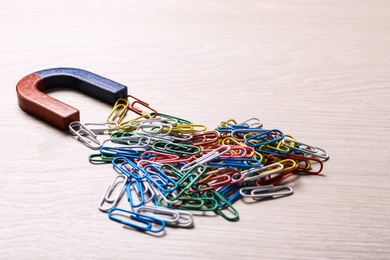 Magnet attracting colorful paper clips on light wooden background