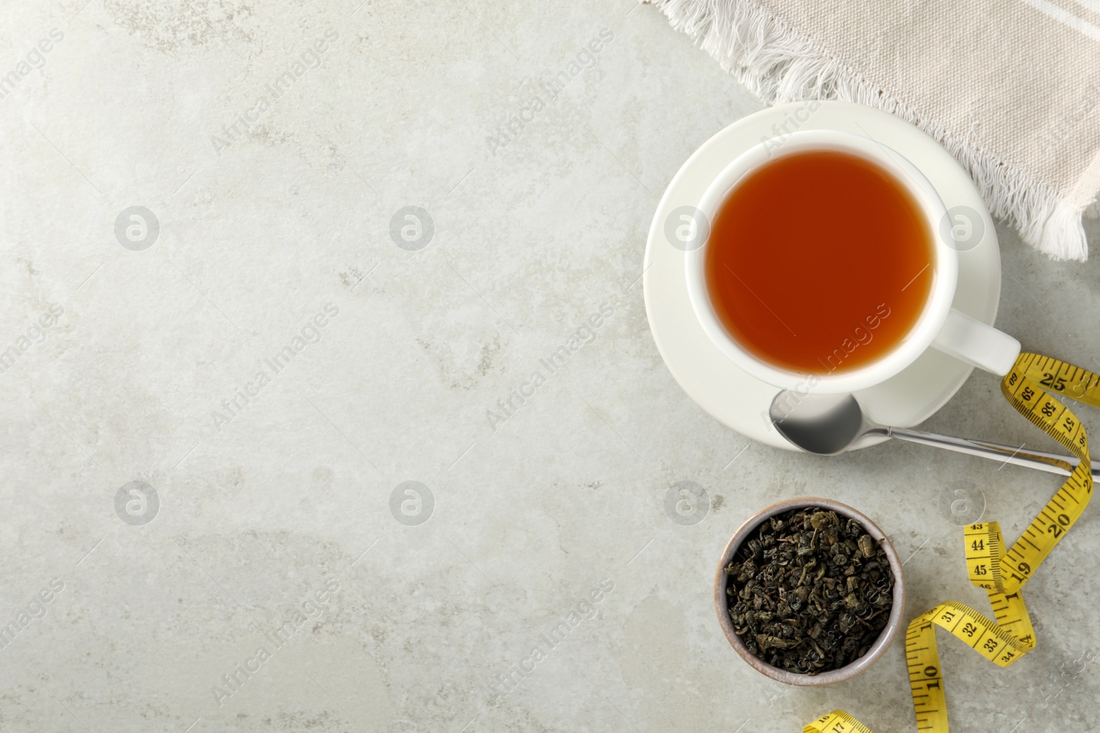 Photo of Cup of herbal diet tea and measuring tape on white table, flat lay with space for text. Weight loss concept