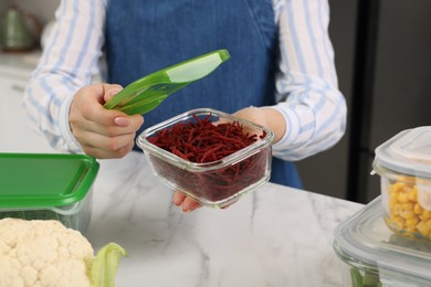Woman holding open container with cut fresh red beets at white marble table in kitchen, closeup. Food storage