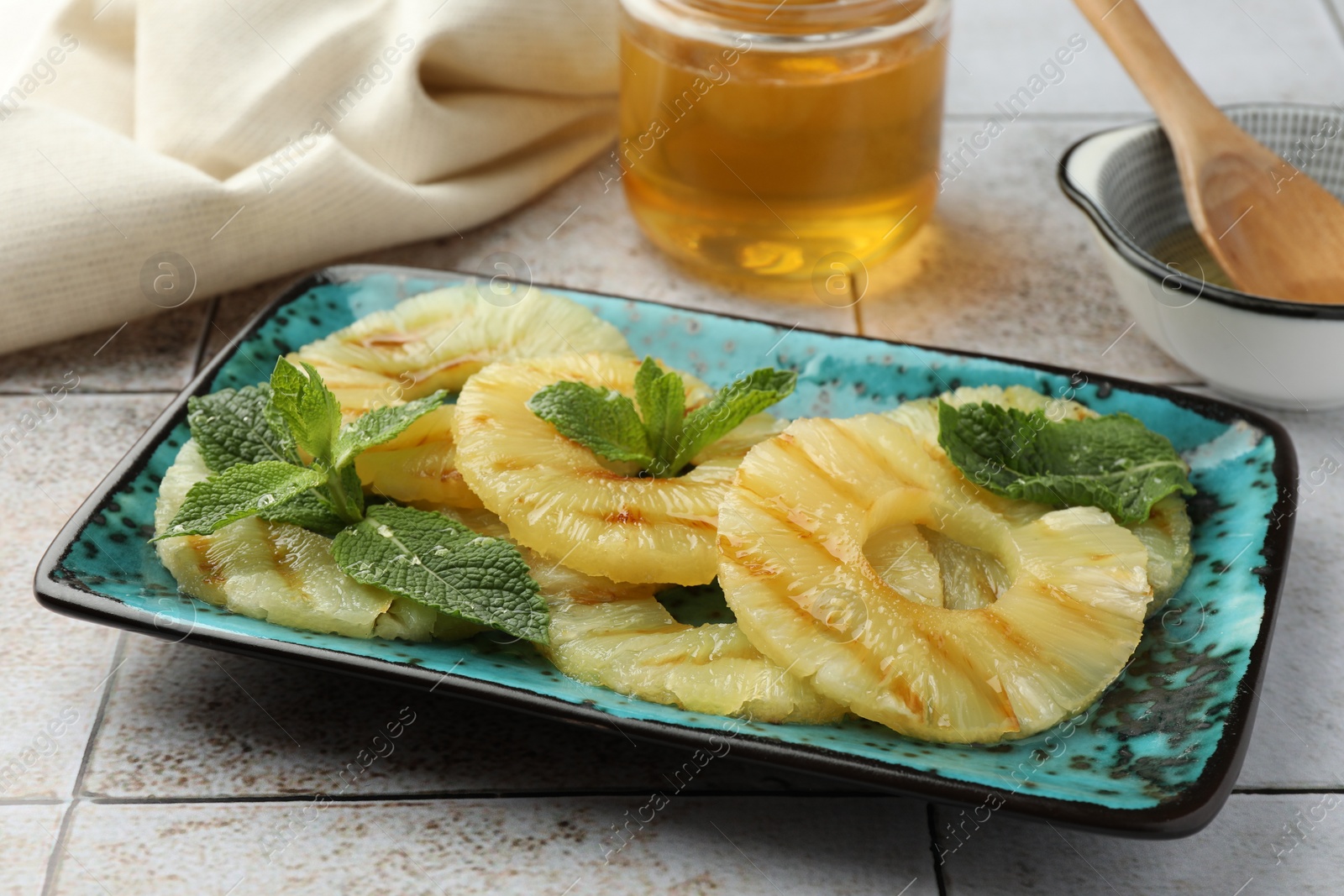 Photo of Tasty grilled pineapple slices with mint on light gray table, closeup