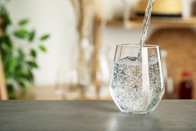 Pouring water into glass on grey table indoors, space for text. Refreshing drink