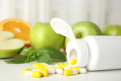 Bottle with vitamin pills and fruits on white table, closeup