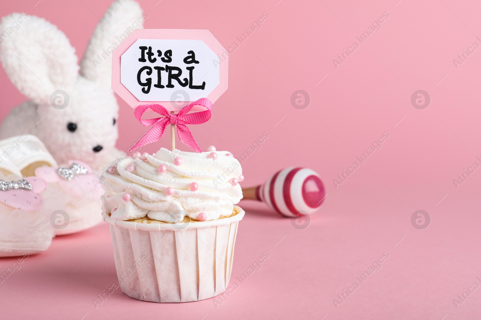 Photo of Beautifully decorated baby shower cupcake with cream and girl topper on pink background. Space for text