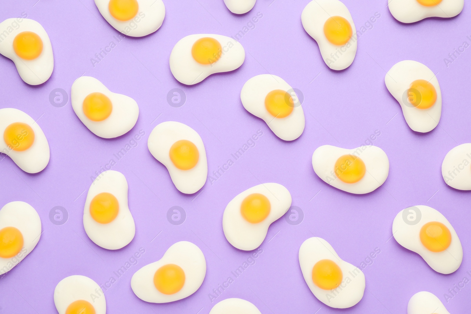 Photo of Tasty jelly candies in shape of egg on lilac background, flat lay