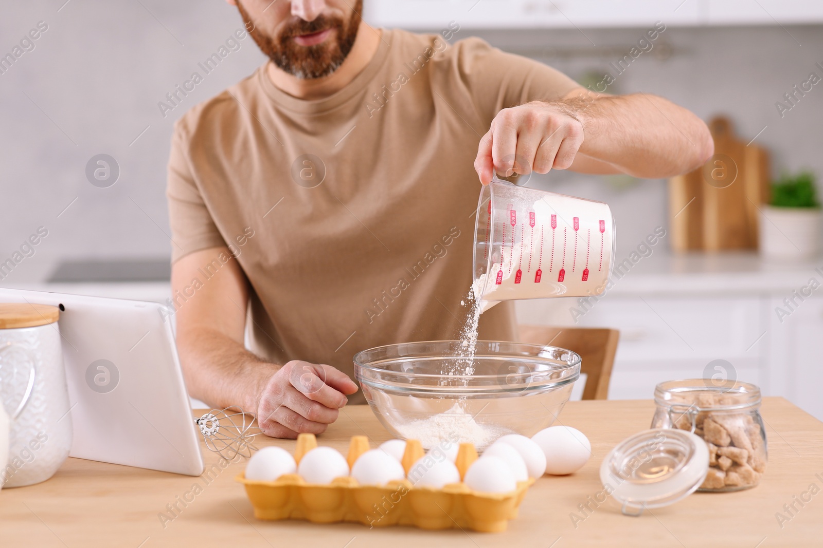 Photo of Man making dough while watching online cooking course via tablet in kitchen, closeup